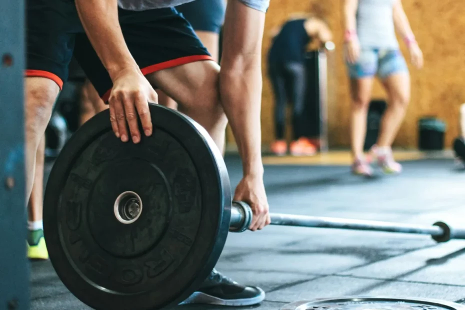 Musculation : les fondamentaux avant de commencer. Un athlète saisit une barre olympique avec des poids dans une salle de sport, prêt à soulever pour son entraînement.